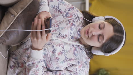 Vertical-video-of-Young-woman-listening-to-music-on-sofa-at-night.-Enjoyable-and-happy.